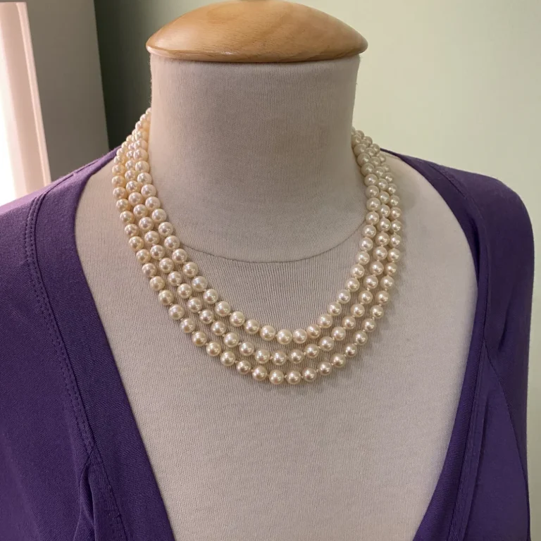 Perlenkette aus drei Reihen, elegant um den Hals drapiert, auf einem Mannequin.