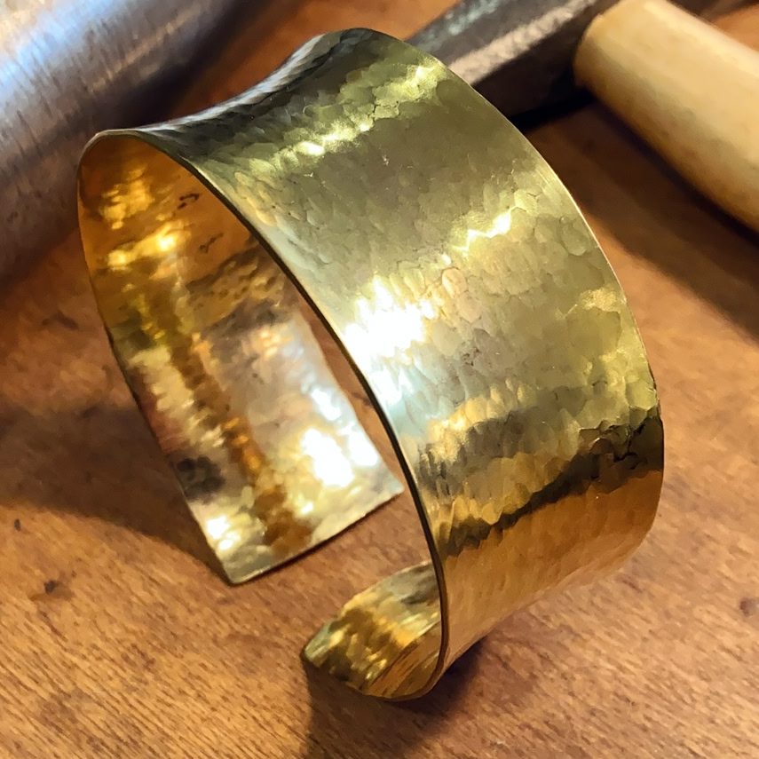 Goldene, handgefertigte Armspange mit glänzender und strukturierter Oberfläche.