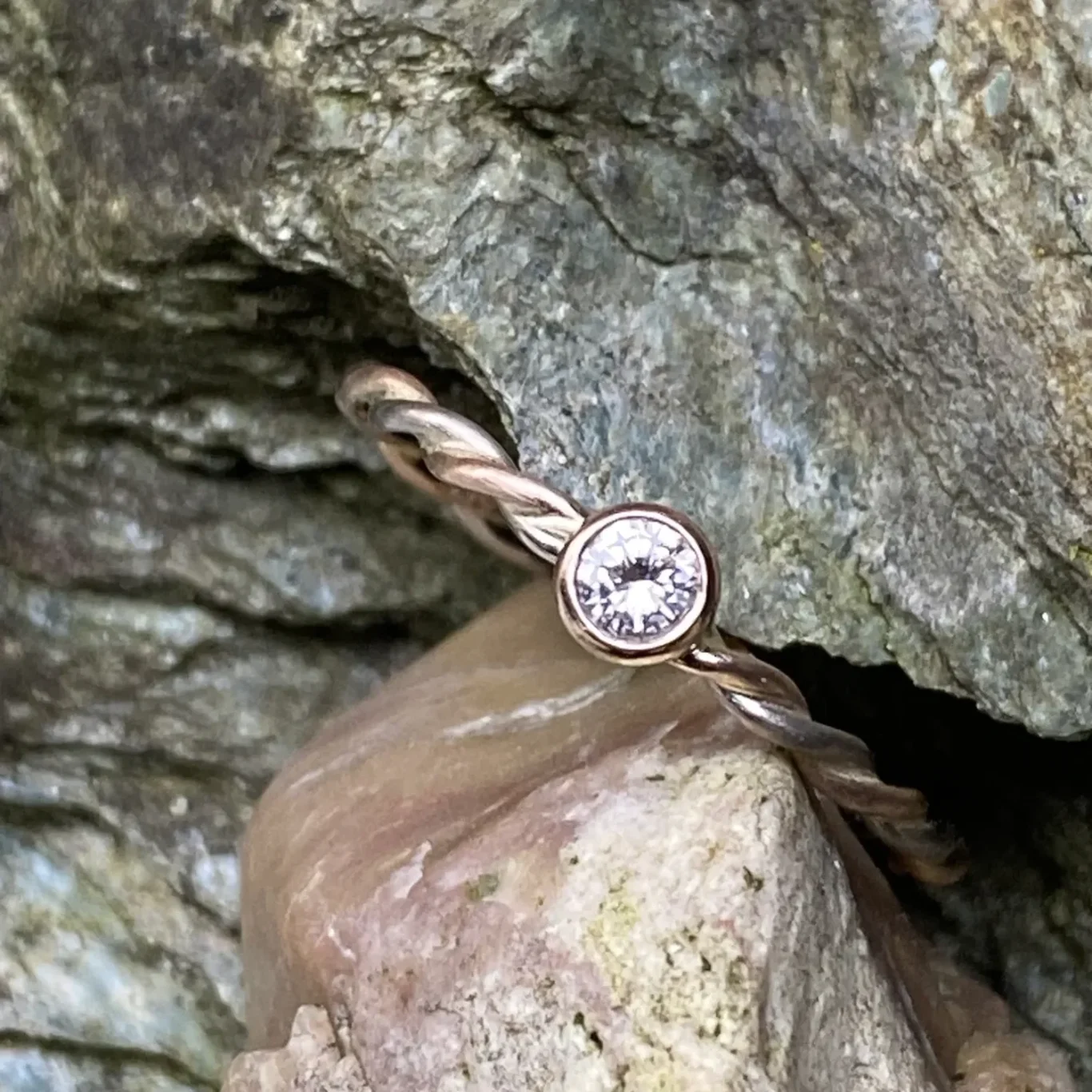 Ring aus zwei Golddrähten geflochten, mit Brillant auf steinigem Untergrund.