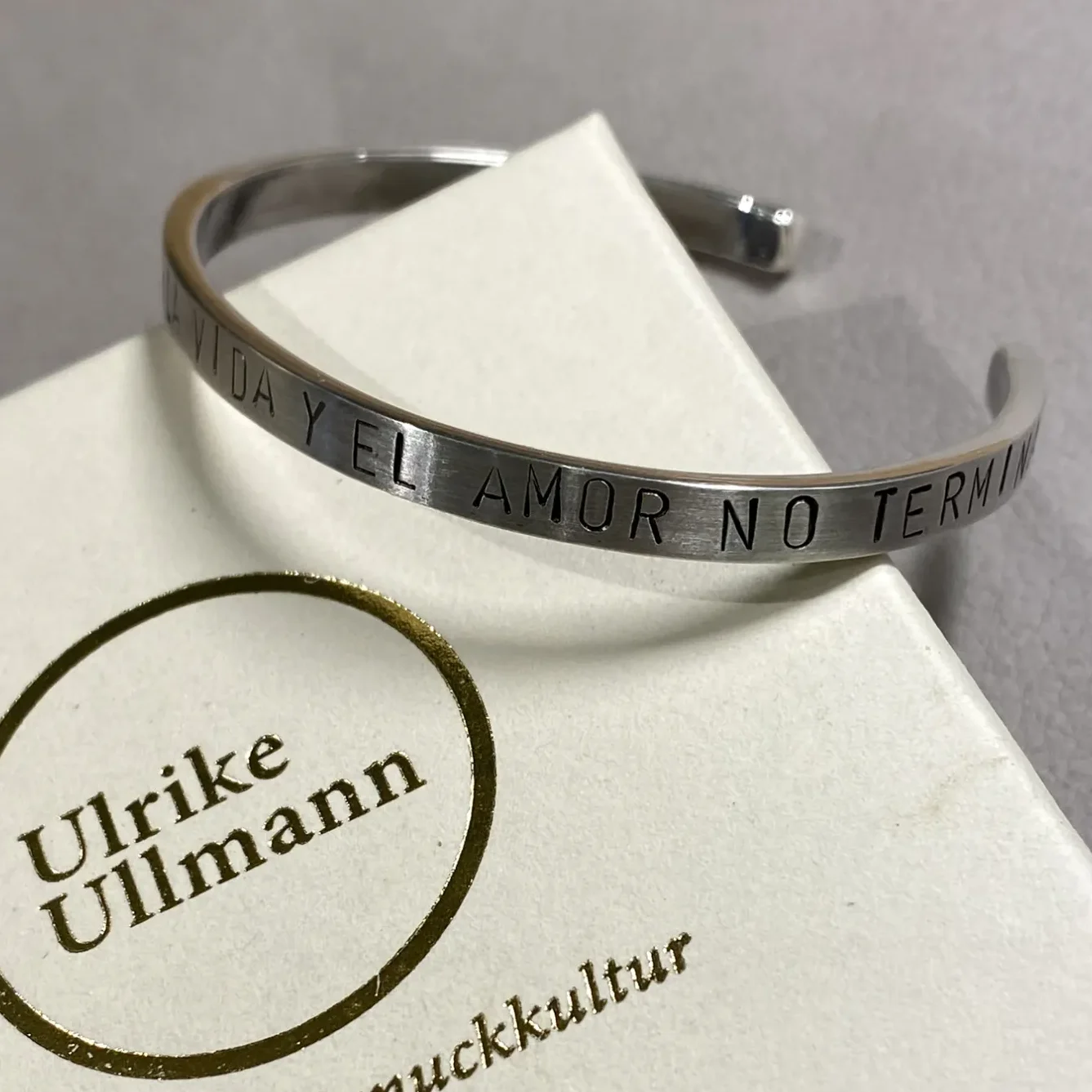 Silberner Armspange mit eingraviertem Text, daneben eine Box mit dem Namen Ulrike Ullmann.