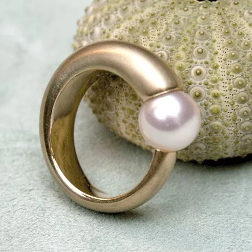 Goldener Ring mit einer runden Perle, auf einer strukturierten Oberfläche platziert.