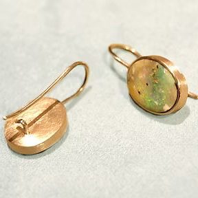 Zwei goldene Ohrringe mit ovalen Anhängern mit Opalen.