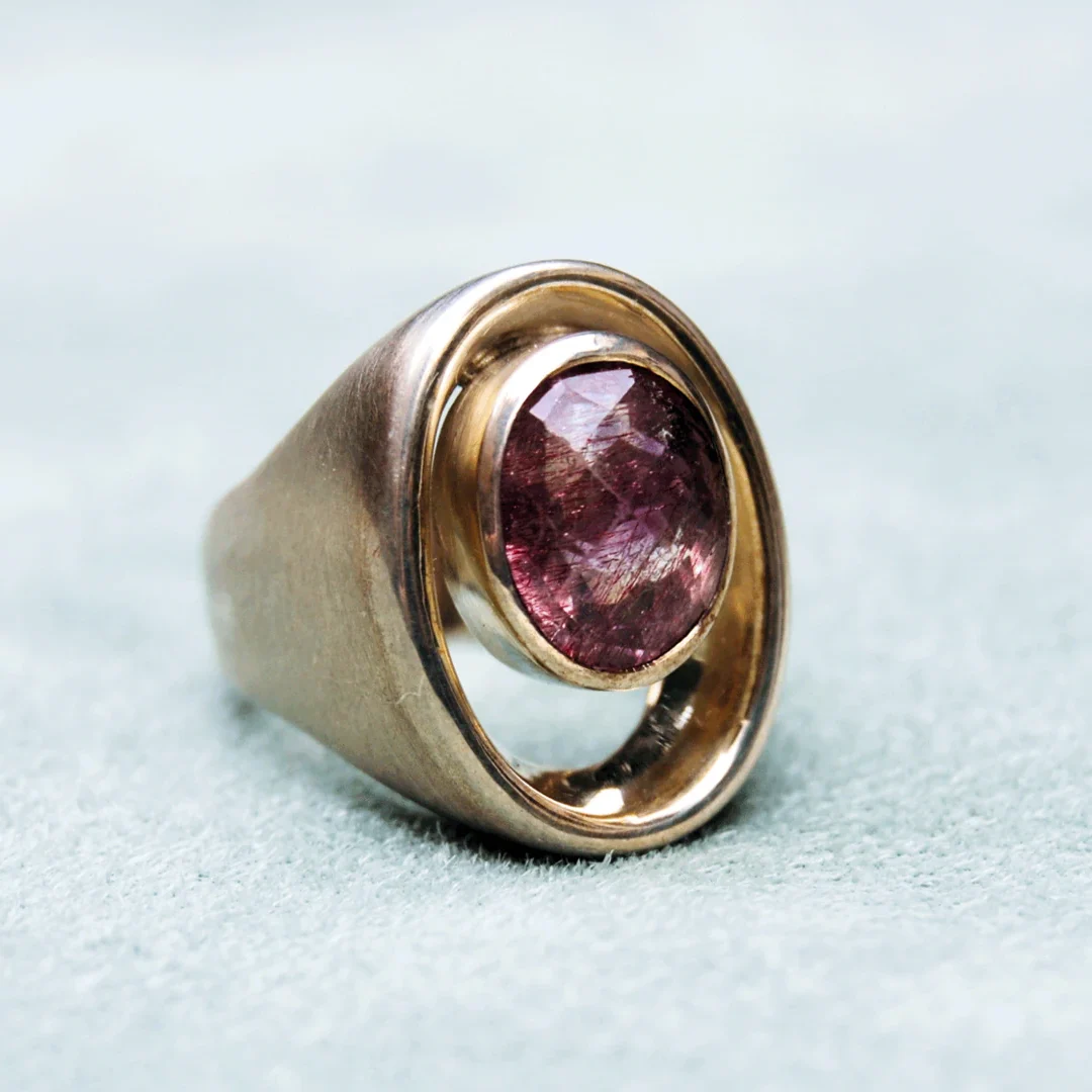 Goldener Ring mit ovalem, rosa Stein in einer modernen Fassung.