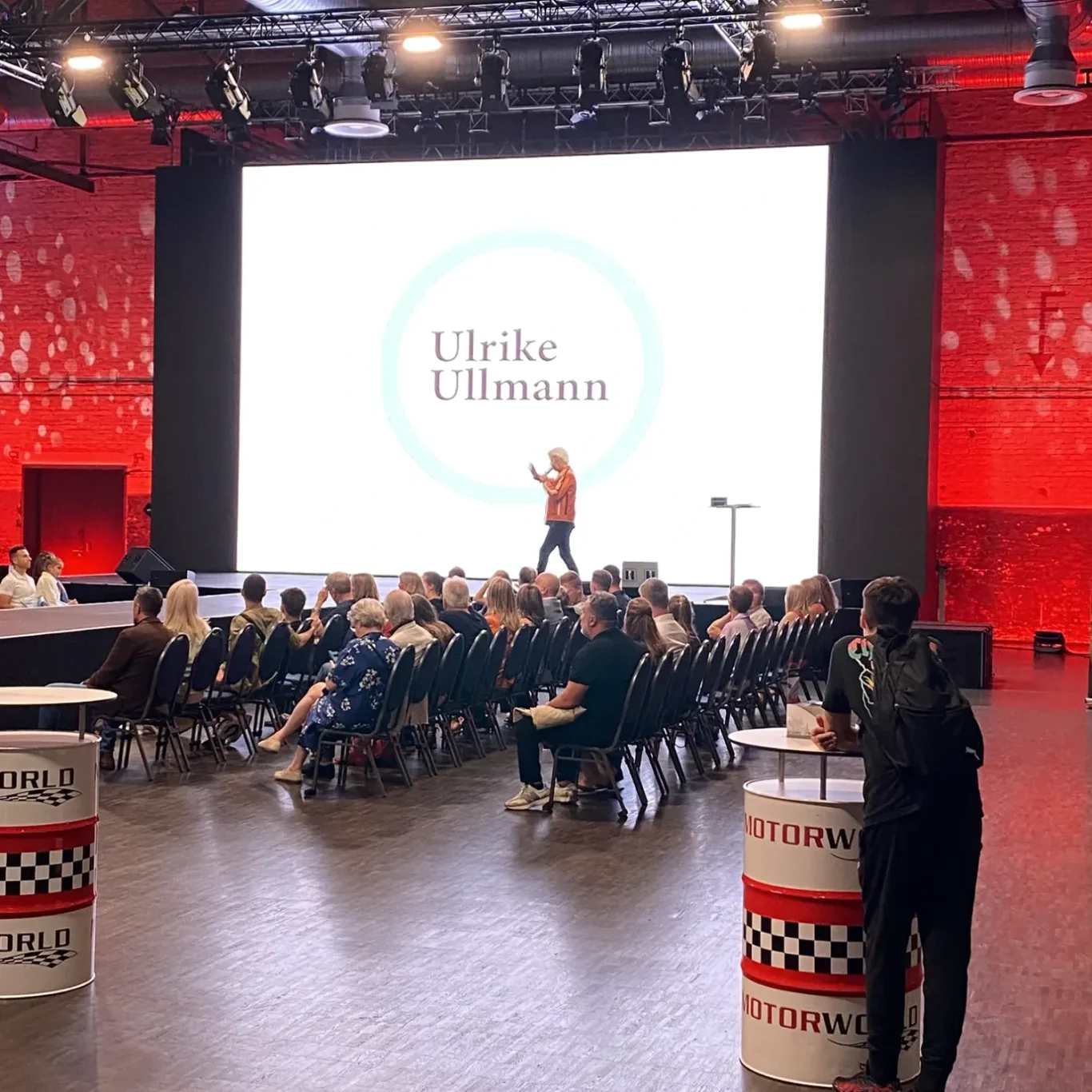 Eine Präsentation auf einer großen Bühne vor einem Publikum in einem modernen Veranstaltungssaal.