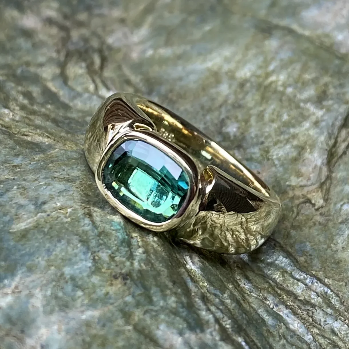 Goldener Ring mit rechteckigem, grünem Turmalin auf einer strukturierten Oberfläche.