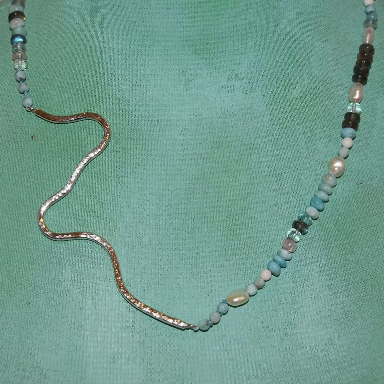 Eine lange Kette aus bunten Perlen und einem geschwungenen Silberanhänger in Form des Rheins bei Rhodenkirchen.