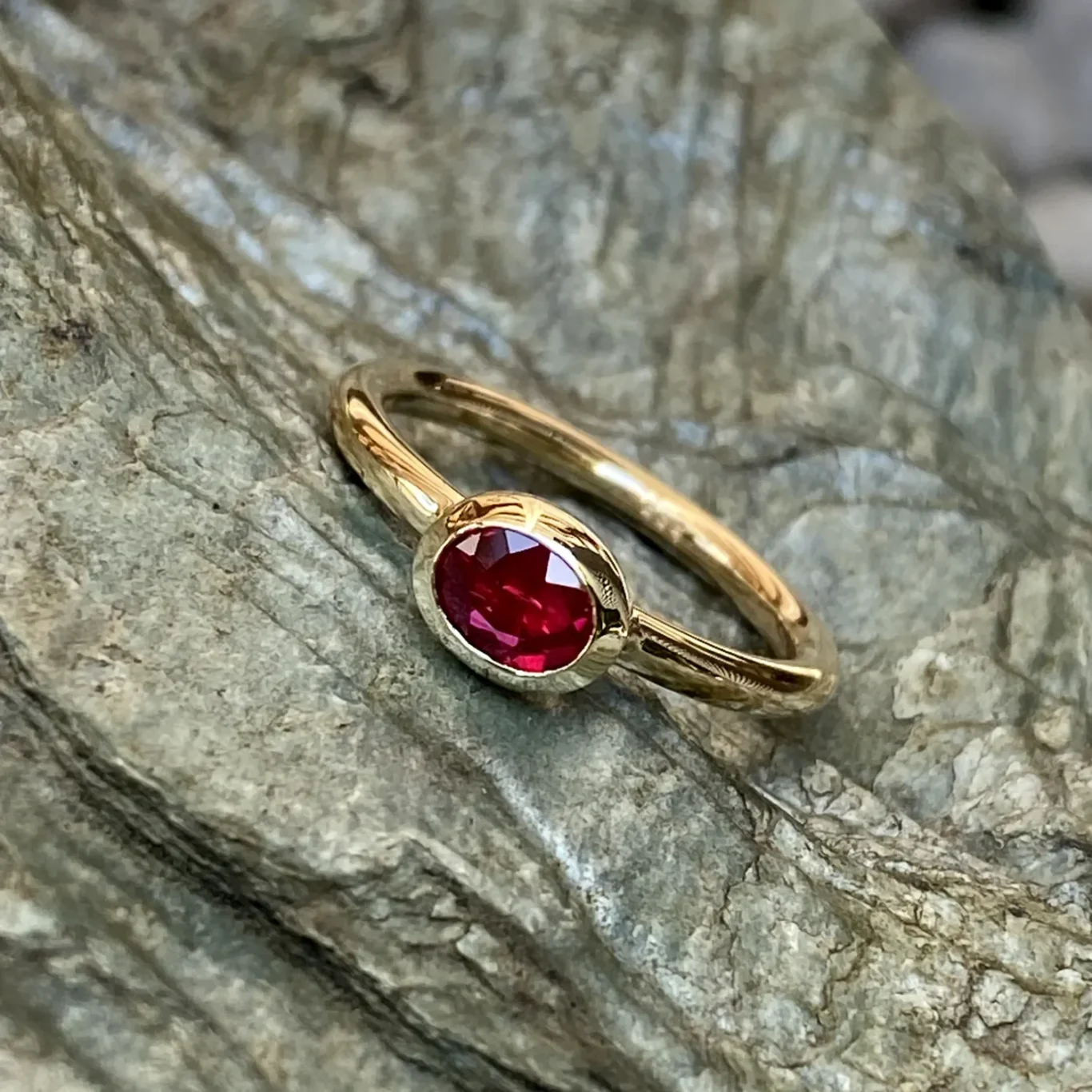 Ein goldener Ring mit einem ovalen, roten Rubin auf grauem Stein.