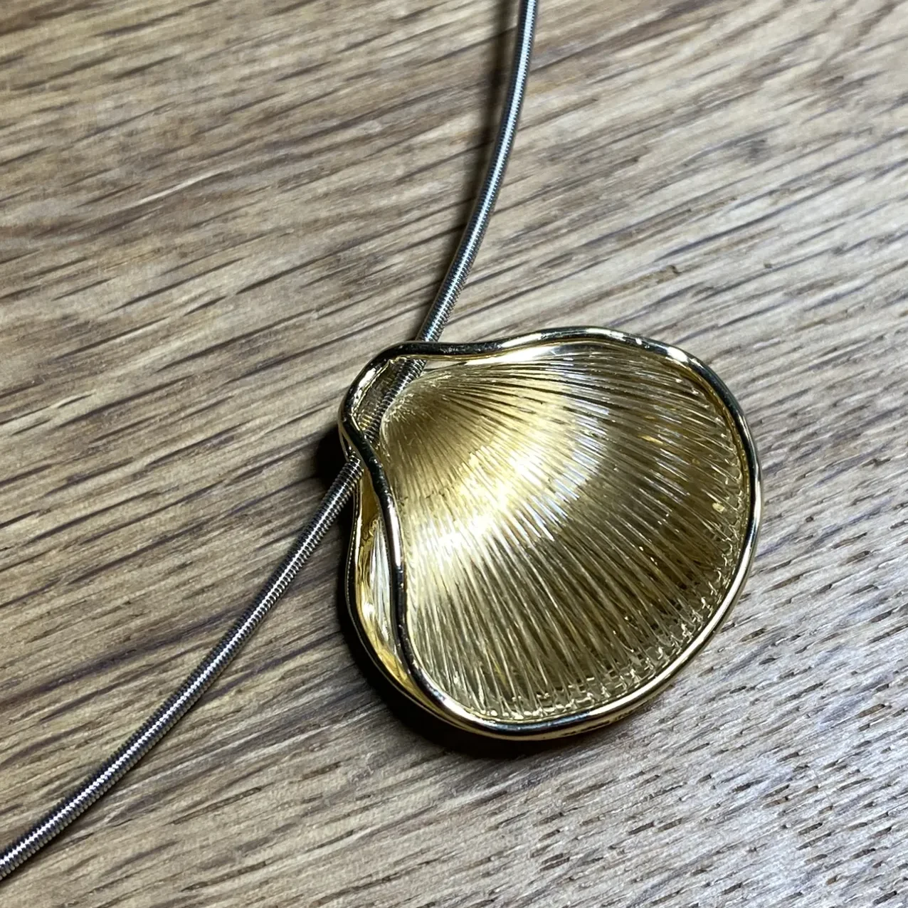 Goldfarbener Muschelanhänger an einer goldenen Halsschnur.