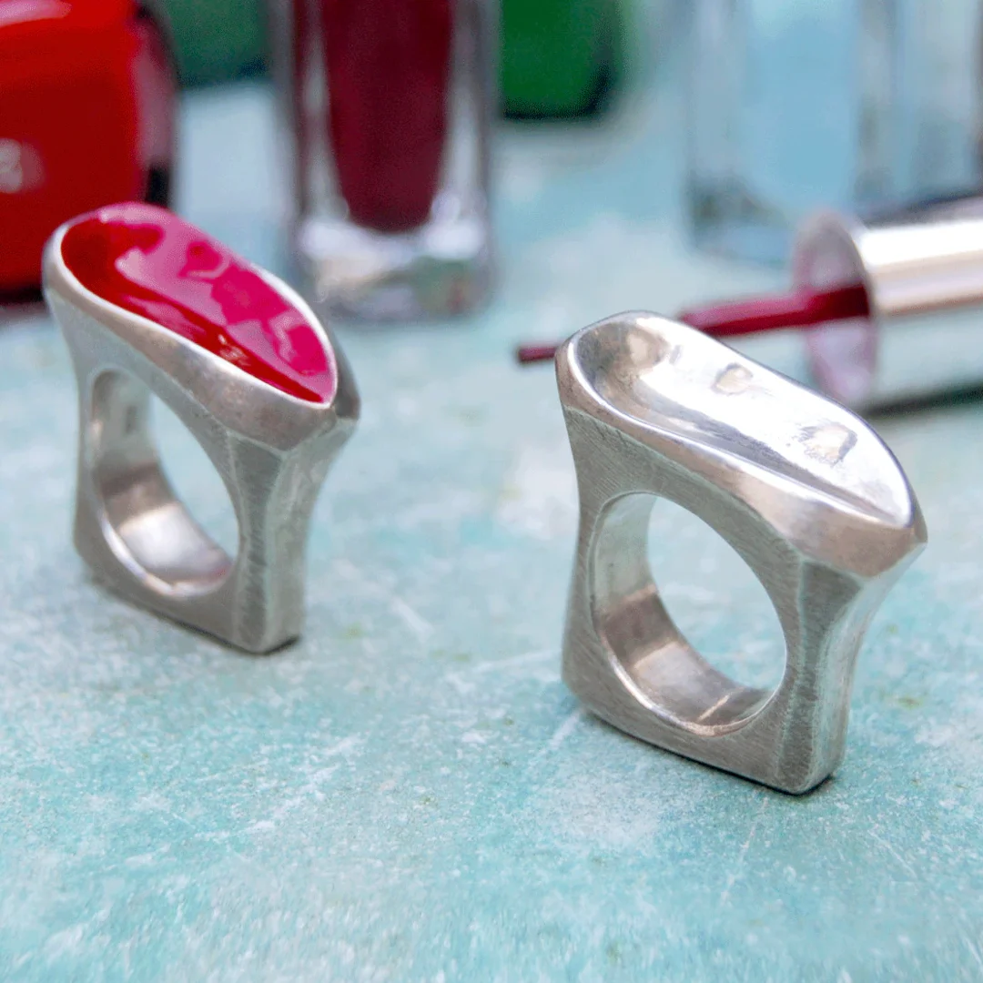 Zwei moderne Ringe aus Silber, einer mit rotem Nagellack bemalt.