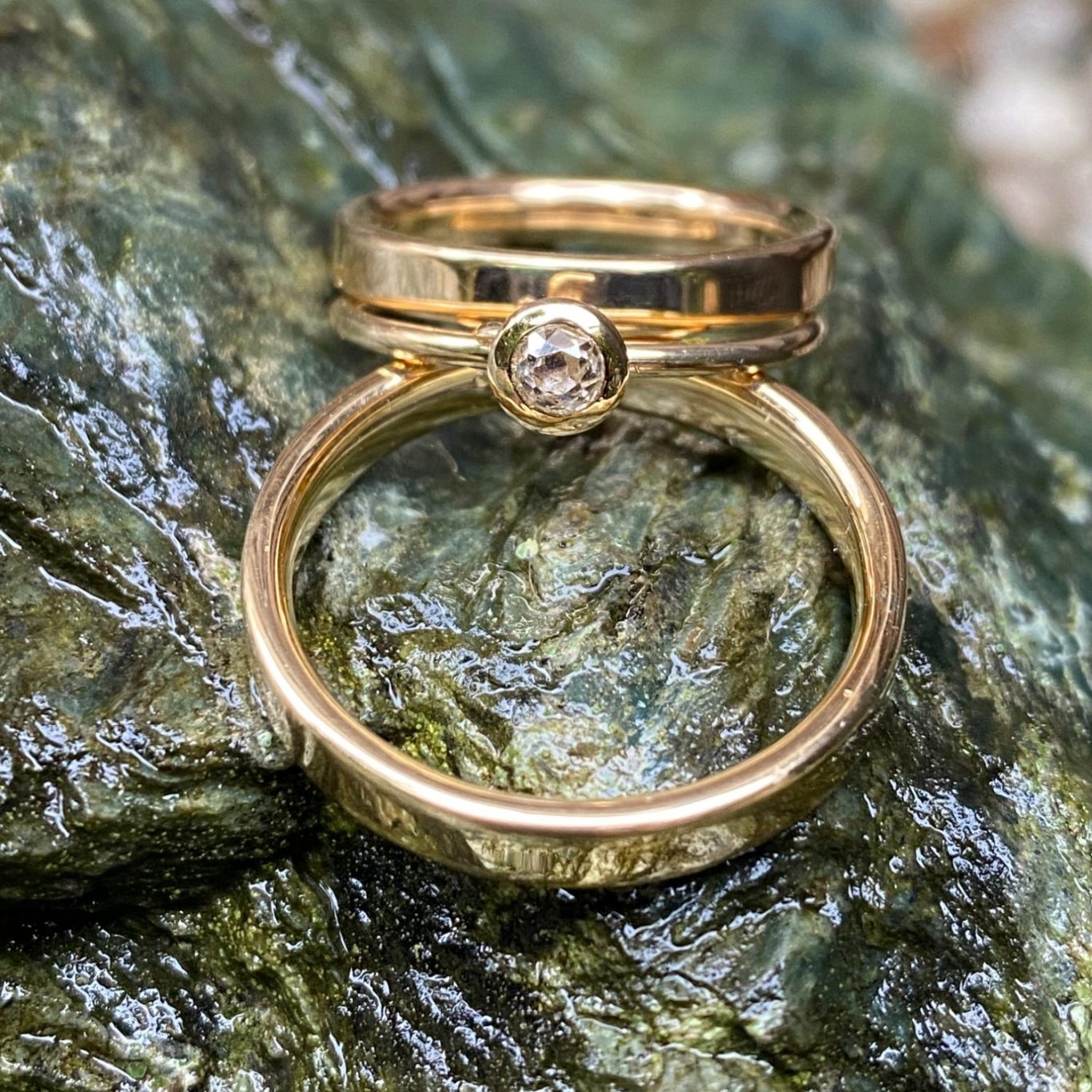 Goldene Ringe mit einem kleinen Diamanten, auf einer rauen Felsoberfläche platziert.