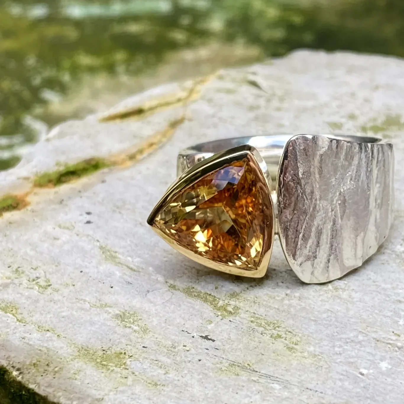 Silberner Ring mit triangelförmigem gelbem Stein in Goldeinfassung.
