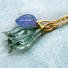 Halskette mit transparent blassgrüner Blume und lila Tropfenanhänger.