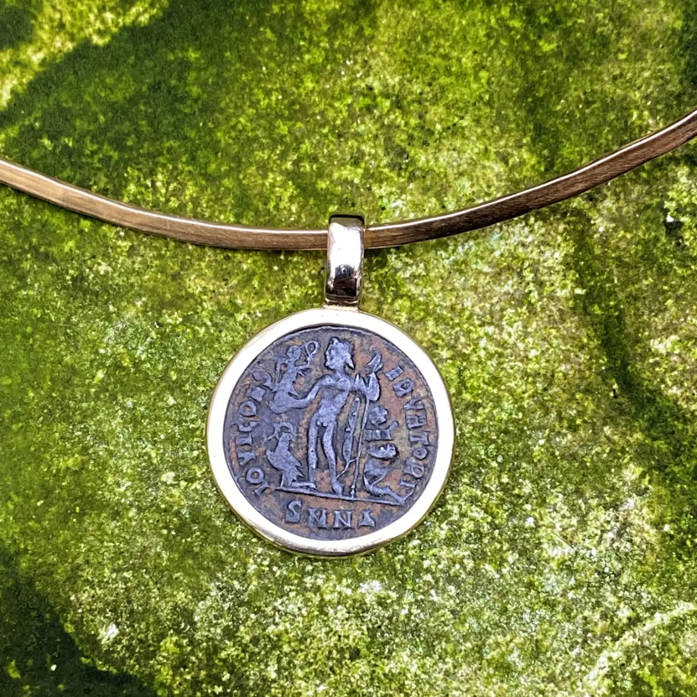 Eine goldene Halskette mit einer runden Bronze-Münze als Anhänger in Goldfassung.