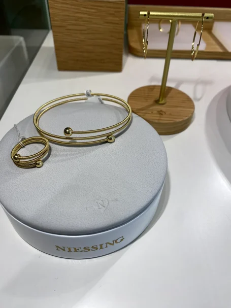 Goldschmuck auf einem grauen Schmuckkissen, mit Armreif und Ring daneben.