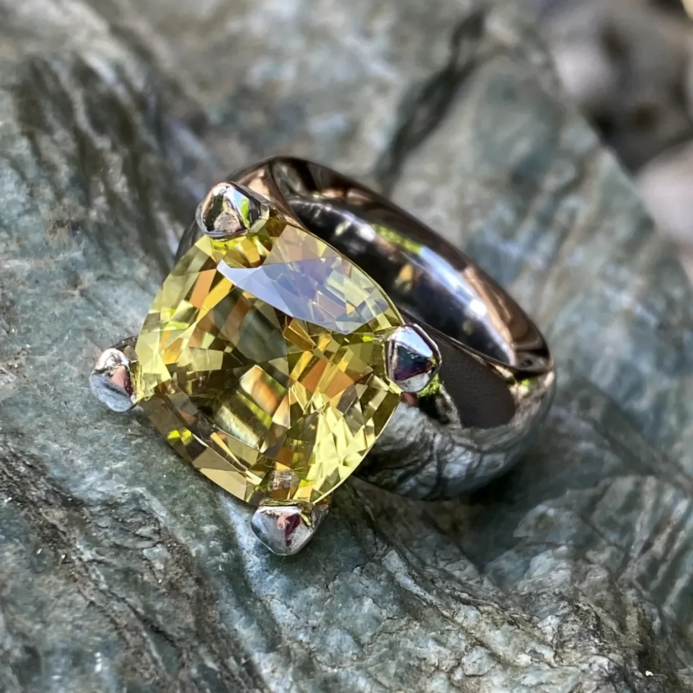 Ein breiter Weißgoldring mit einem großen, gelben, facettierten Edelstein.