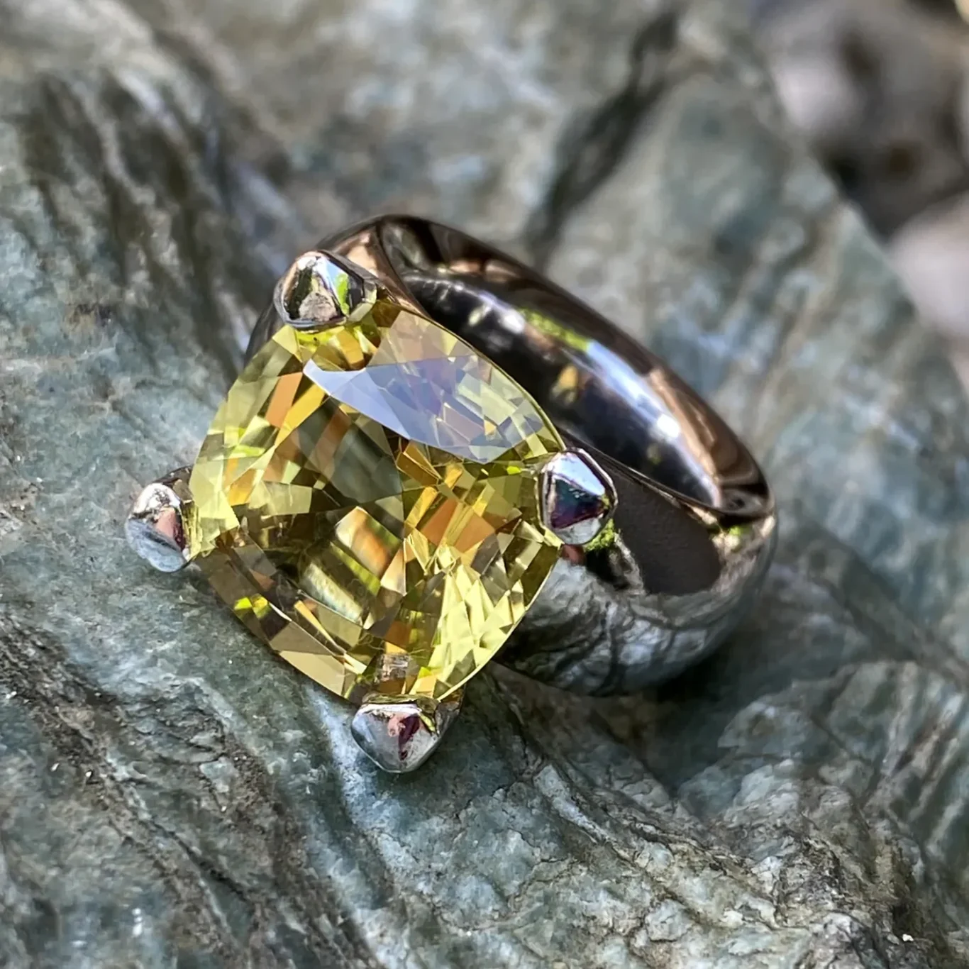 Breiter Weißgoldring mit großem, gelbem Edelstein auf grauem Untergrund.