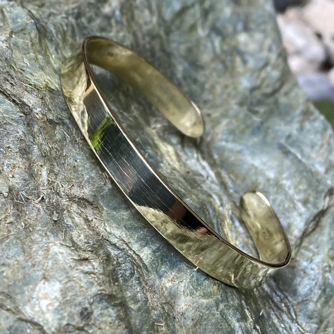 Goldfarbene Armspange mit glatter Oberfläche auf steiniger Unterlage.