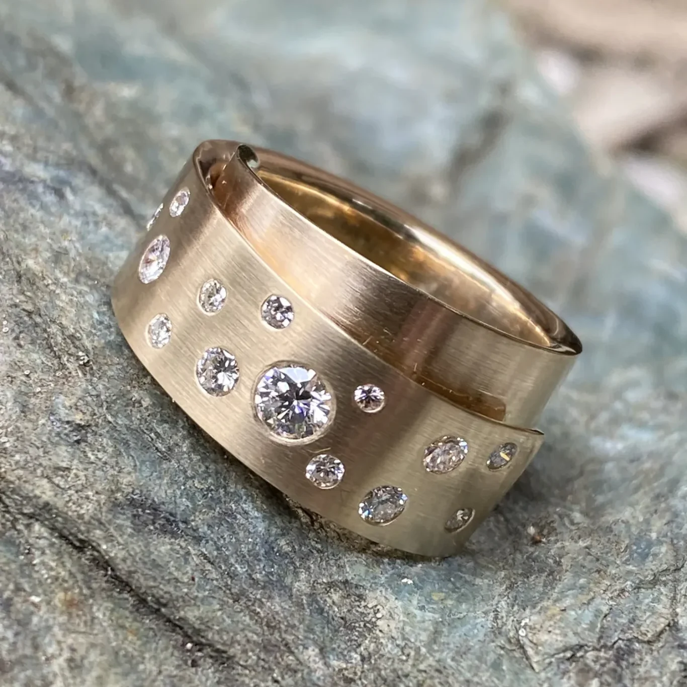 Goldring, mit Brillanten besetzt, auf einem steinigen Untergrund platziert.