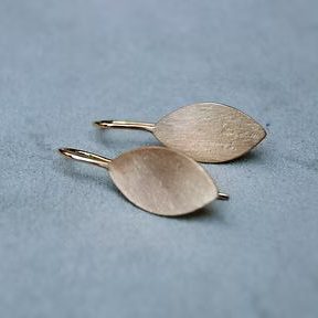 Zwei ovale Ohrringe aus goldenem Metall auf einer grauen Oberfläche.