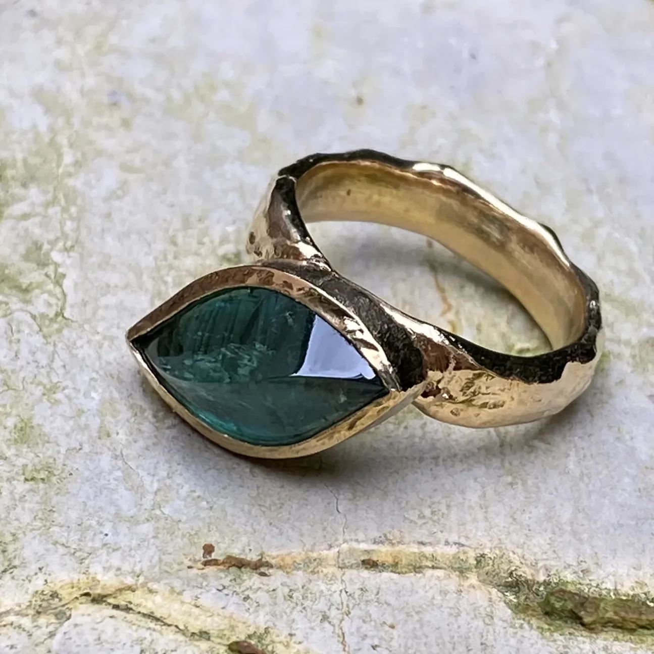 Goldener Ring mit grünem Blattförmigem Stein.