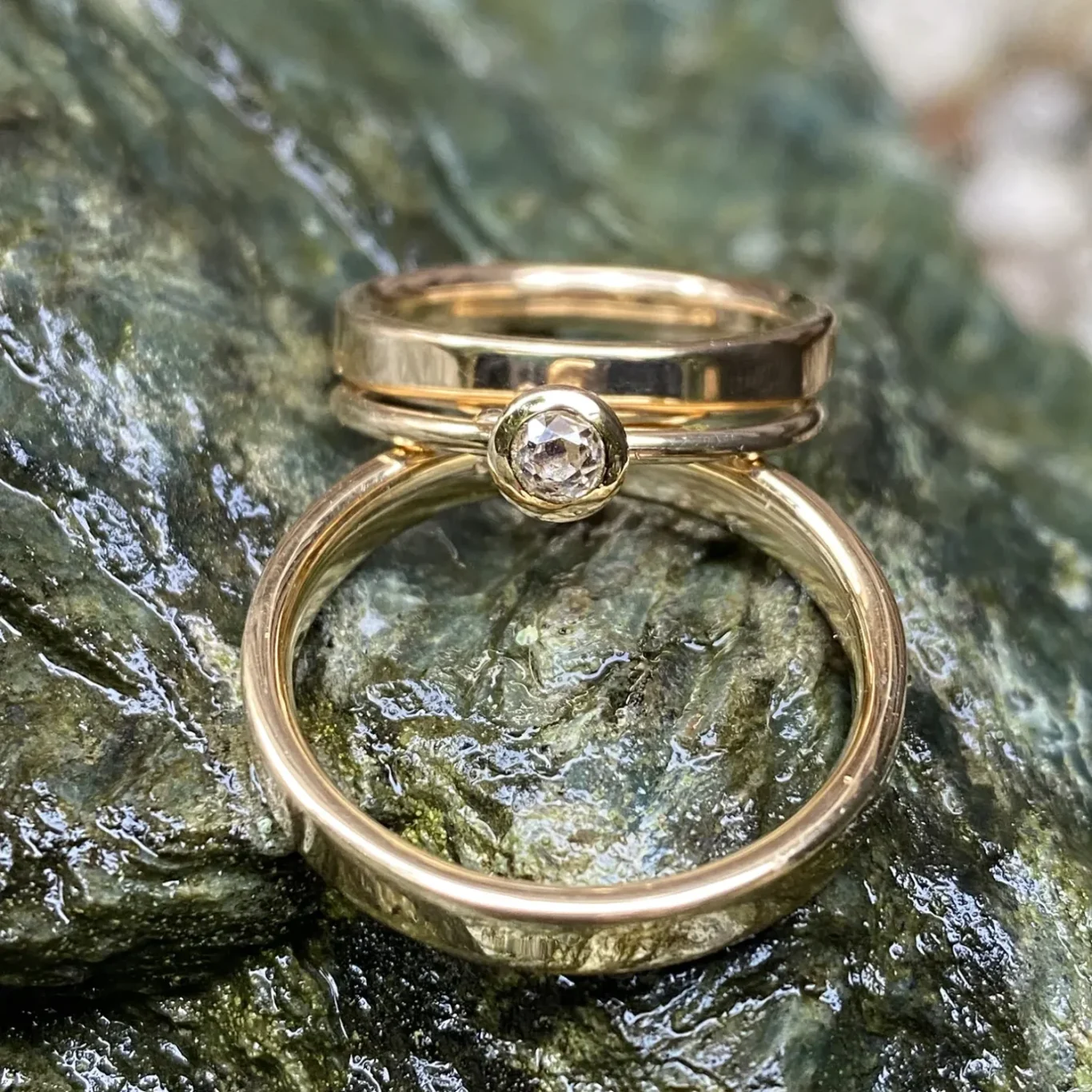 Zwei goldene Trauringe und ein Beisteckring liegen übereinander auf einer steinigen Oberfläche.