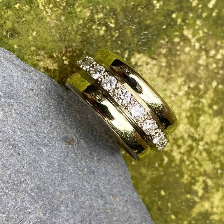 Ein Goldring aus zwei alten Trauringen gefertigt mit in der mittleren Reihe angeordneten Brillanten, an einem grauen Stein platziert.